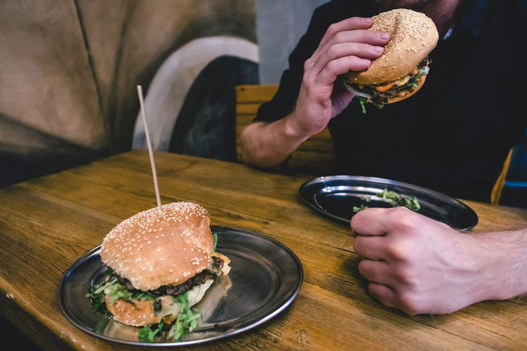 Midsection of man eating burger while sitting in restaurant