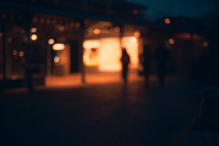 Defocused image of silhouette people on illuminated street at night
