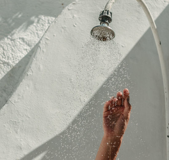 Cropped hand of person under shower head against wall