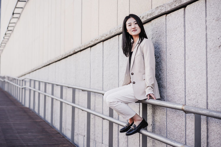 Confident beautiful chinese business woman sitting on railing in city