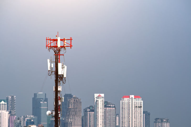 Communication transmitter tower on backdrop of city view and sky , cellular station with antenna.