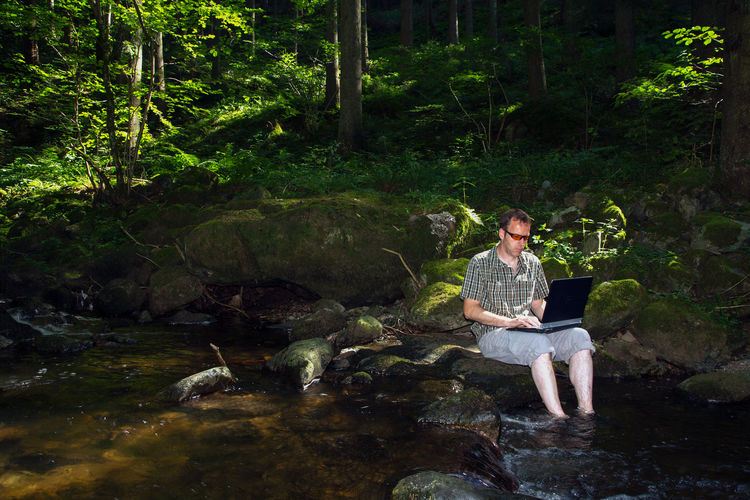 Men sitting on rock by river in forest