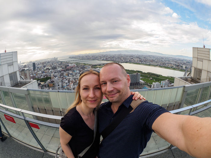 Fish-eye lens view of couple standing at observation point against cityscape