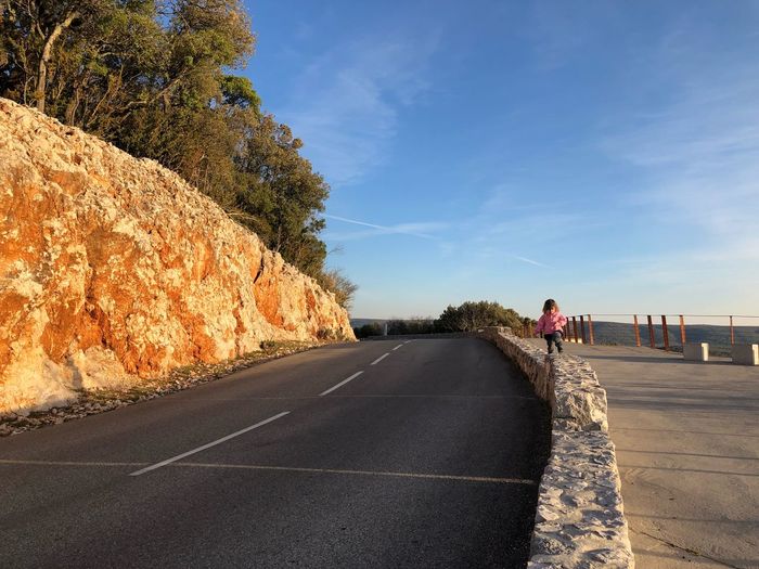 Girl walking on retaining wall against blue sky