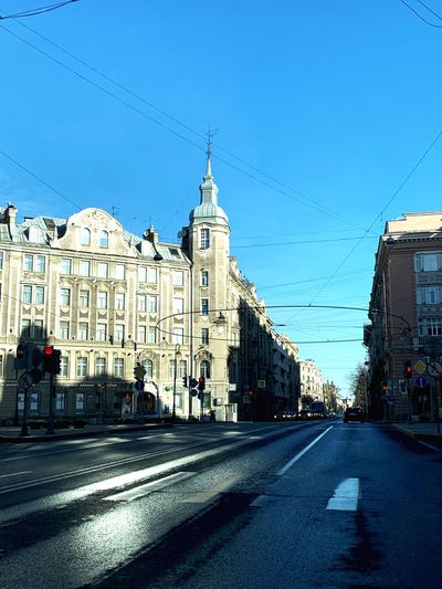 Road by buildings against clear blue sky