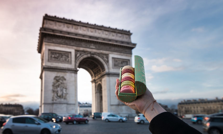 Cropped hand of woman holding colorful macaroons against triumphal arch