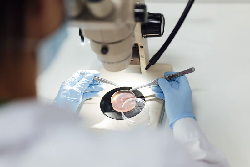 Mature female medical expert using tweezers while analyzing medical samples through microscope in lab