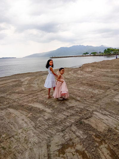 Siblings walking on the beach against sky