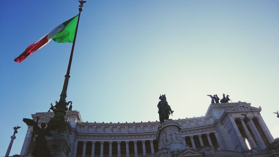 Low angle view of italian flag by altare della patria against clear sky