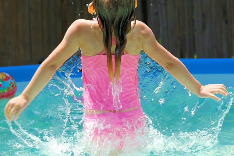 Rear view of girl with arms outstretched in wading pool