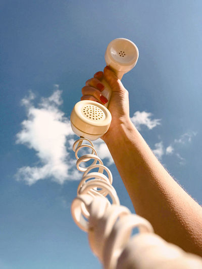 Cropped hand of woman holding telephone against blue sky
