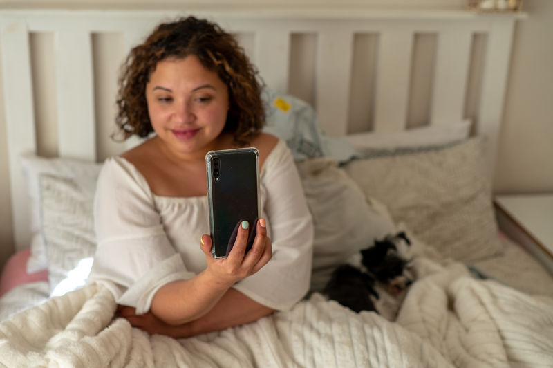 Young woman using phone while lying on bed at home