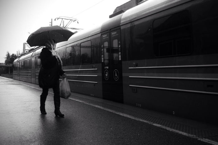 Woman carrying umbrella looking at train