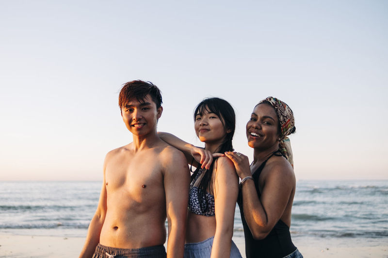 Smiling man with female friends standing at beach during sunset