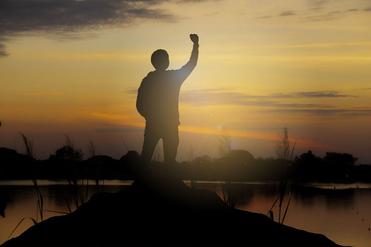 Silhouette man standing by lake against sky during sunset