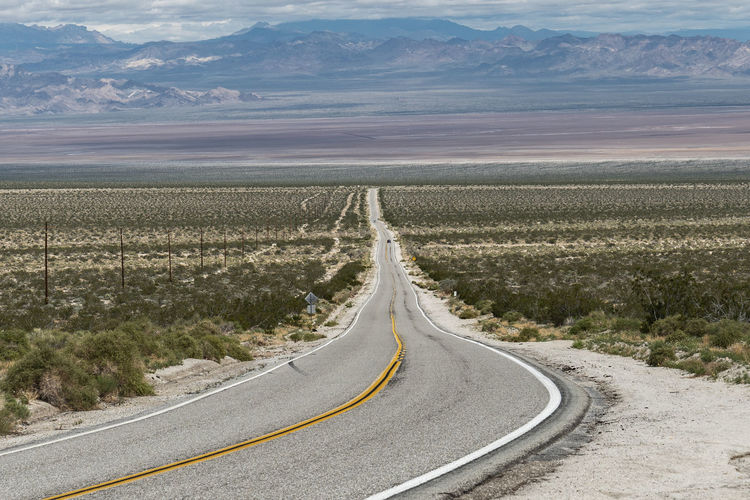 Country road amidst landscape against sky