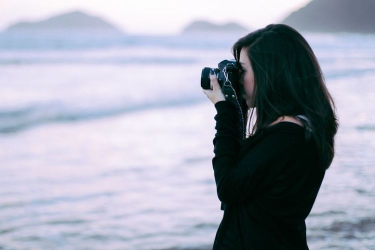 Side view of young woman photographing at beach