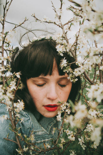 Portrait of young woman with flowers against tree