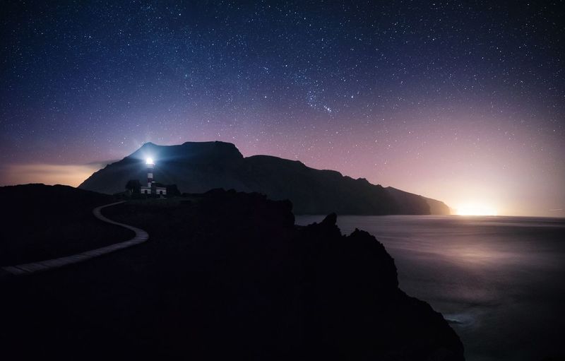 Silhouette mountains by sea against star field at night