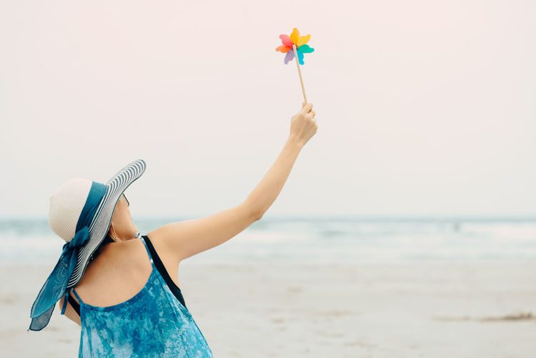 Woman holding umbrella at beach against sky