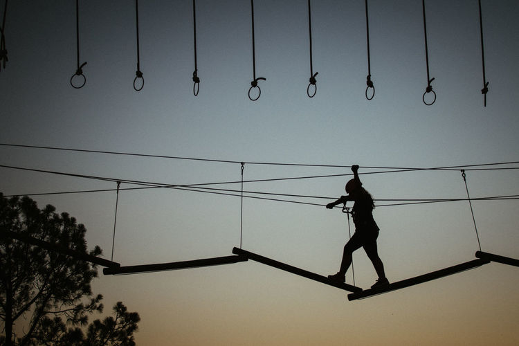 Low angle view of silhouette man hanging on rope against sky