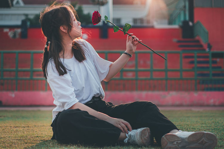 Full length of woman sitting on grass while holding rose