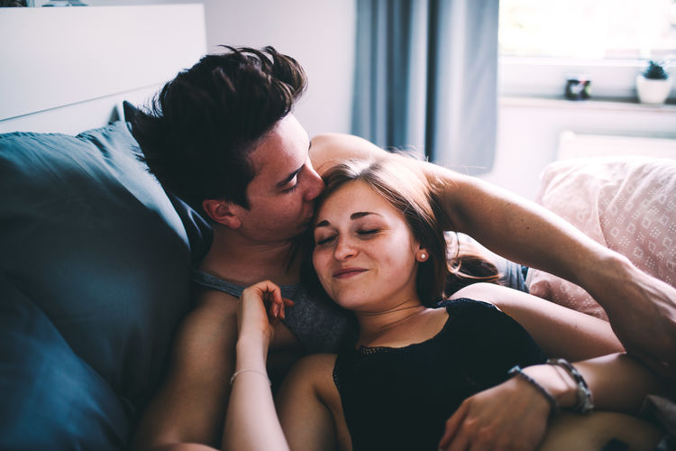 High angle view of smiling young man kissing woman sleeping on bed at home
