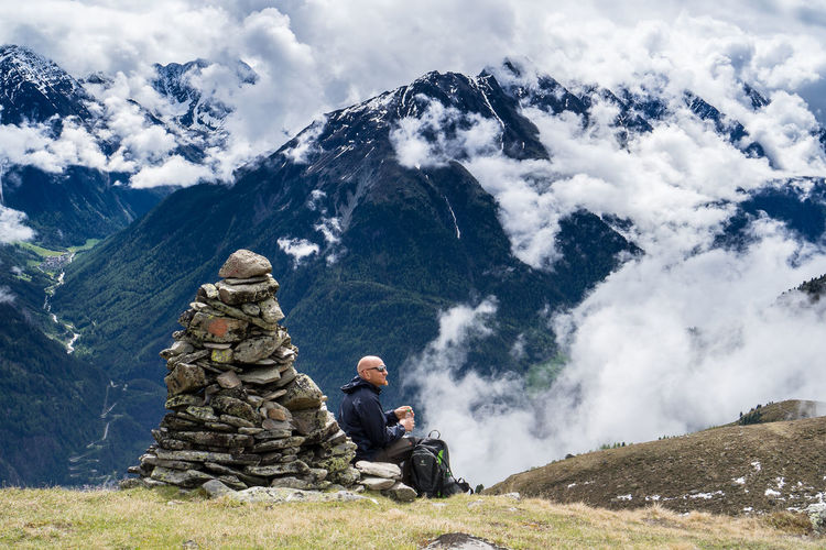 Rear view of man sitting on rock against mountains