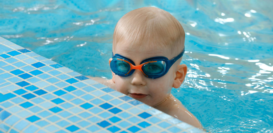 Toddler child learning to dive in indoor swimming pool with teacher physical activity for kids