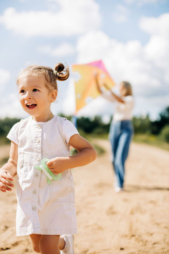 A little girl in a white dress is running along the road with a string of a kite in her hand
