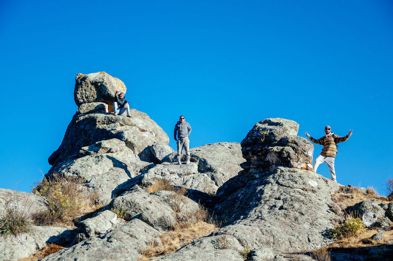Low angle view of people on rock against clear blue sky