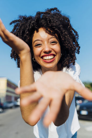 Happy young woman with curly hair gesturing on sunny day