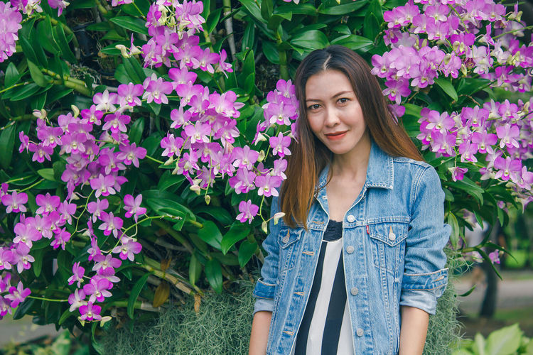 Portrait of beautiful young woman standing by purple flowering plants