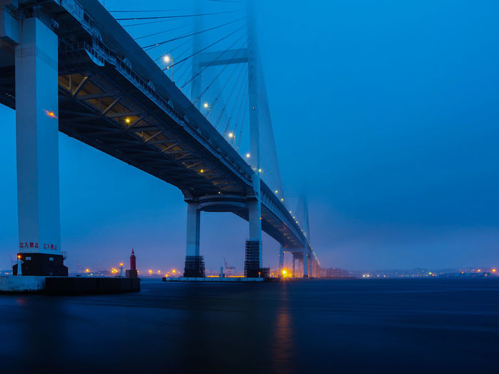Illuminated bridge over bay in port of yokohama against sky at dawn on a foggy morning.