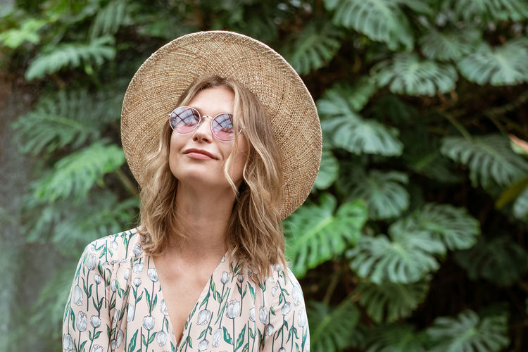 Beautiful young woman in a straw hat and glasses in the park on a background of greenery