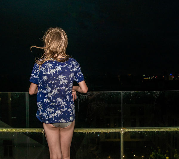 Rear view of a boy standing in a balcony at night