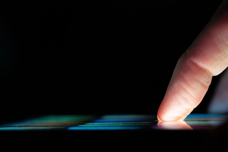Close-up of hand touching illuminated light over black background