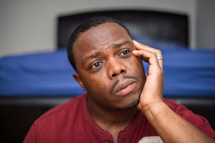 Young depressed or anxious african american man in bedroom at home sitting