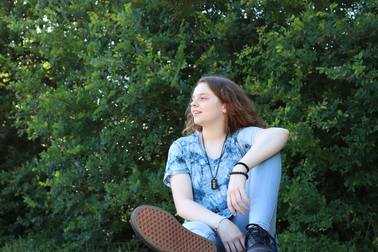 Young woman looking away while sitting on tree