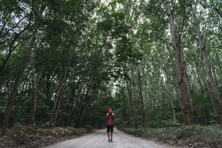 Man standing on road amidst trees against sky
