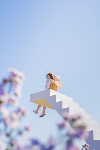 Asian woman relax and hold umbella on white stair in flower garden on springtime vacation