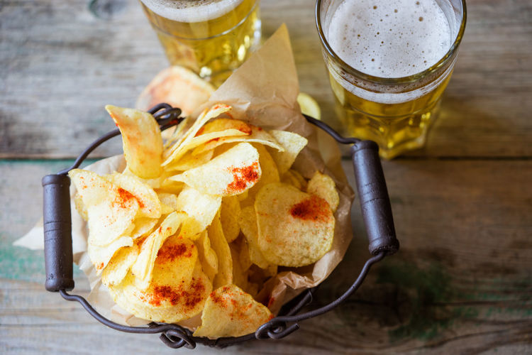 High angle view of fresh crunchy potato chips with beer on table