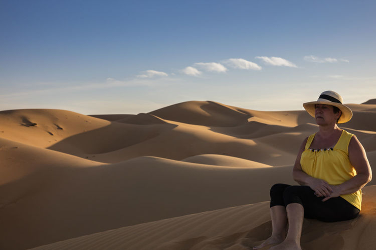 Senior woman sitting at desert against clear sky during sunny day