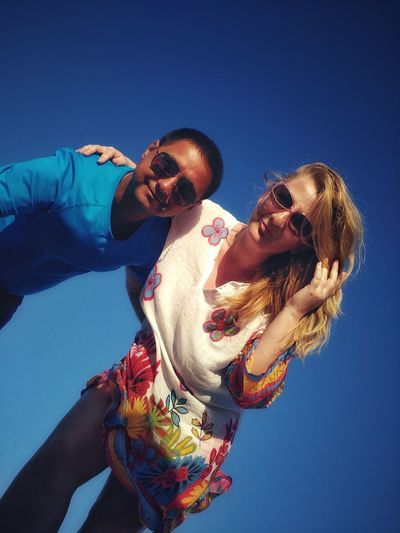 Low angle portrait of couple wearing sunglasses standing against clear blue sky
