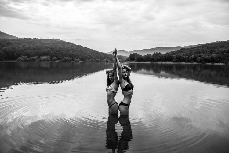 Portrait of young women standing in lake against sky