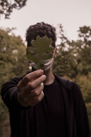 Man wearing mask holding leaf standing outdoors