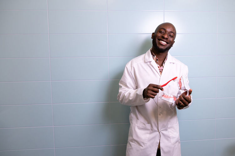Portrait of dentist standing against wall