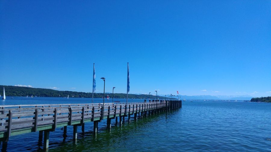 Pier over sea against clear blue sky