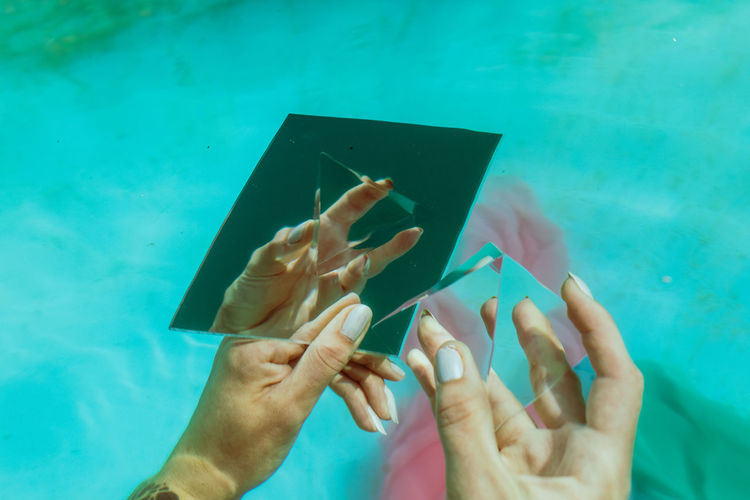 Cropped hand of woman holding pyramid crystal and mirror in swimming pool
