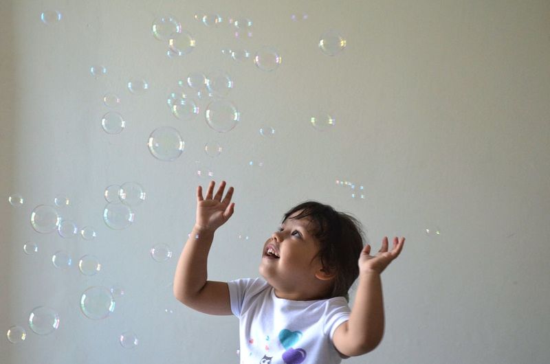 Cute girl playing with bubbles against wall